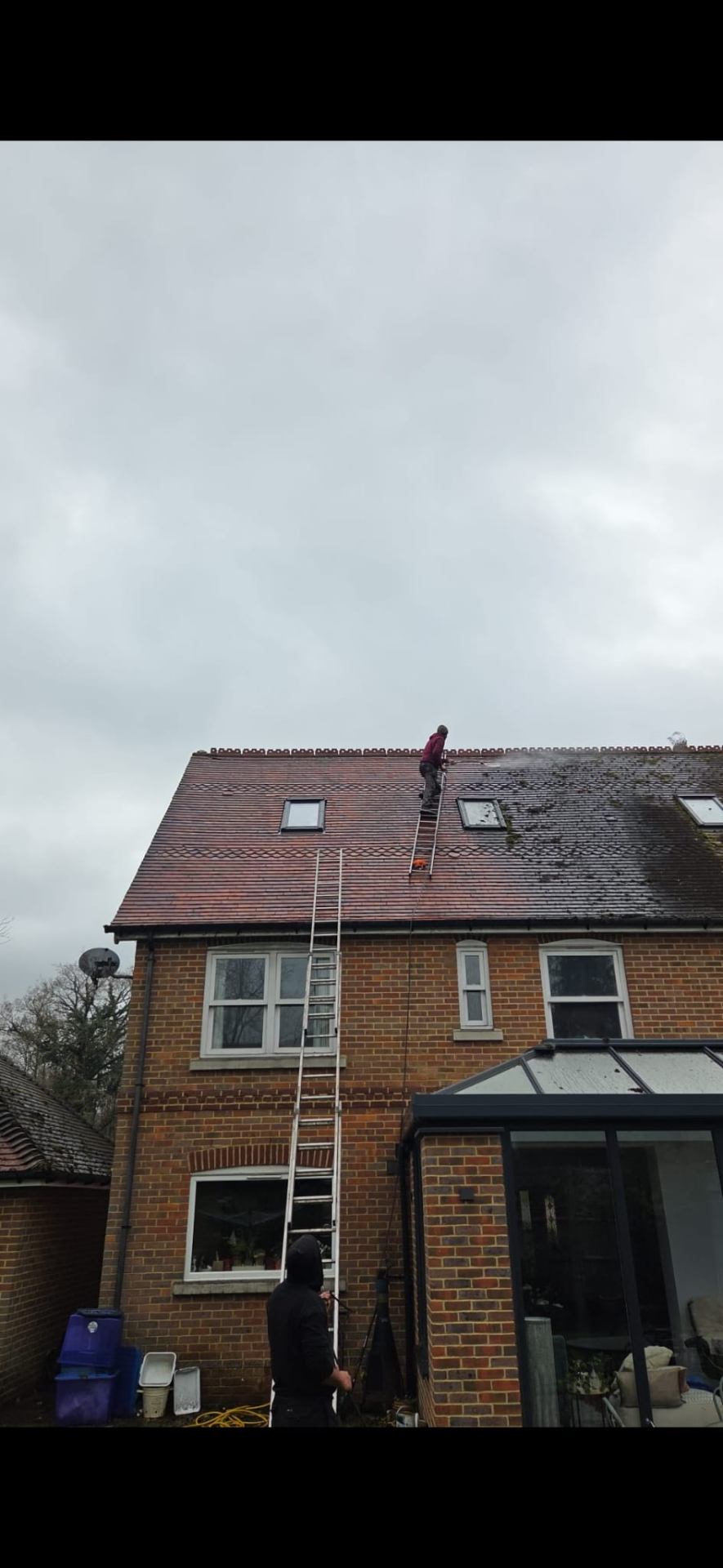 Operative softwashing a tiled roof on a brick home